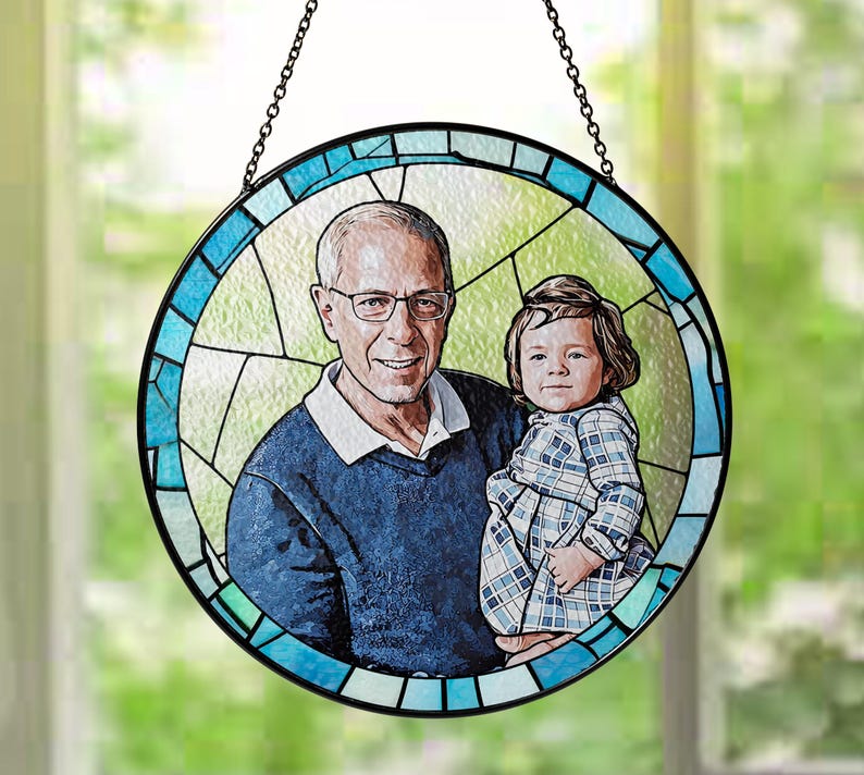 May include: A stained glass round hanging ornament with a blue and white border. The ornament features a portrait of a man and a young child. The man is wearing a blue shirt and the child is wearing a plaid dress.