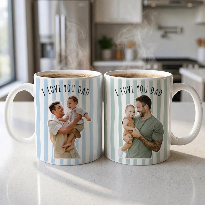 May include: Two white ceramic mugs with a blue and white striped pattern. Each mug features a photo of a father and child, with the text "I LOVE YOU DAD" in black. The mugs are filled with a dark liquid, possibly coffee.