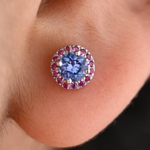 May include: A close-up of a blue gemstone earring with a halo of pink gemstones set in silver.