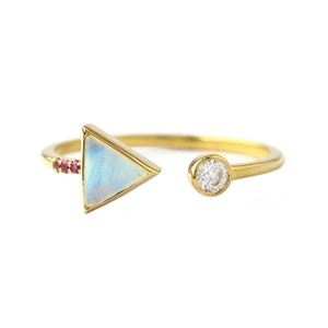 May include: Gold ring with a triangular moonstone and a small round diamond. The ring has a row of tiny red gemstones on one side.