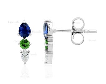 May include: A pair of stud earrings with a vertical design. Each earring features a dark blue pear-shaped gemstone at the top, a green round gemstone in the middle, and a white pear-shaped gemstone at the bottom. The earrings are made of silver.