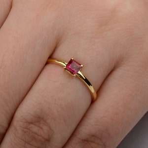 Könnte beinhalten: Ein schlichter Goldring mit einem kleinen, quadratischen, roten Edelstein.