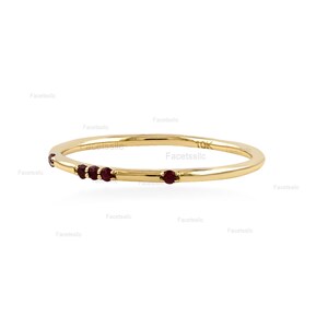 May include: A thin 10k yellow gold band ring featuring four small, round, deep red rubies set along one side. The metal has a polished finish, and the stamp 10k is clearly visible on the inner surface of the gold band.