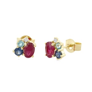 May include: A pair of gold stud earrings featuring a cluster design. Each earring contains one oval-cut red ruby, one round-cut blue sapphire, one round-cut light blue topaz, and one small round-cut white diamond set in yellow gold.