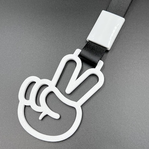 May include: White plastic peace sign keychain with a black lanyard. The peace sign is a simple outline of a hand with two fingers raised.
