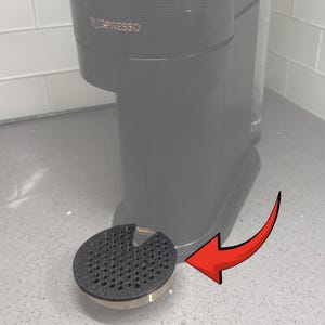 May include: A black and gold coffee machine with the word "NESPRESSO" in gold lettering. A black and gold drip tray is in front of the machine. The drip tray is round with a perforated surface.
