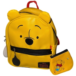 Può includere: Zaino giallo di Winnie the Pooh con portamonete abbinato. Lo zaino presenta il volto di Pooh, dettagli neri e un manico rosso. Il portamonete ha un'illustrazione di Pooh con un barattolo di miele e un'ape. È visibile il logo Disney Winnie the Pooh.