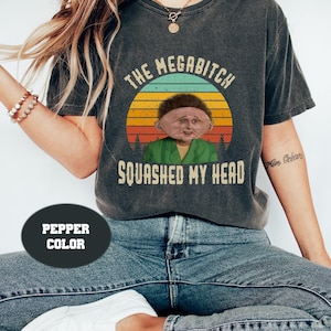 Puede incluir: Una camiseta gris oscuro con un gráfico de estilo vintage de un personaje de dibujos animados con el texto "The Megabitch Squashed My Head".