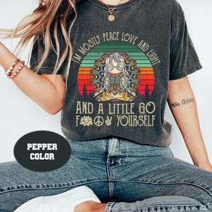 May include: A dark gray t-shirt with a vintage-style sunset graphic and the text "I'm mostly peace love and light and a little go f yourself".