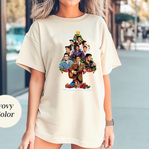 May include: A white t-shirt with a Christmas tree design featuring a collage of Elvis Presley images. The tree is decorated with ornaments and presents. The text "Elvis Christmas" is at the top of the tree.