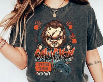 May include: A dark gray t-shirt with a graphic print of Chucky, the killer doll from the Child's Play movie franchise. The graphic features Chucky holding a knife and the text "It's time to play, good guys" and "Your friend to the end".