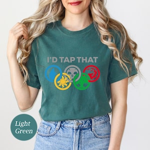 Pode incluir: Uma camiseta verde claro com o texto "I'd Tap That" e cinco s&iacute;mbolos coloridos dispostos em um c&iacute;rculo, que se assemelham aos an&eacute;is ol&iacute;mpicos.