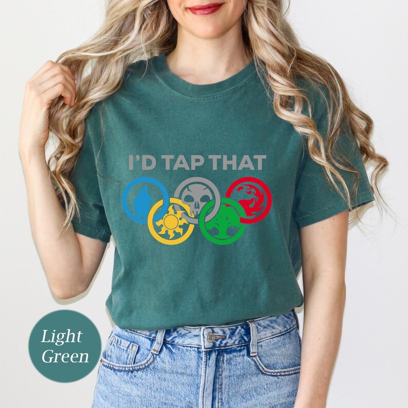 Pode incluir: Uma camiseta verde claro com o texto "I'd Tap That" e cinco s&iacute;mbolos coloridos dispostos em um c&iacute;rculo, que se assemelham aos an&eacute;is ol&iacute;mpicos.