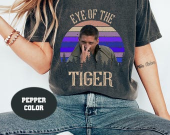 May include: A gray t-shirt with a vintage-style graphic of a man with the text "Eye of the Tiger" in a yellow font. The graphic has a sunset background with purple and blue stripes.