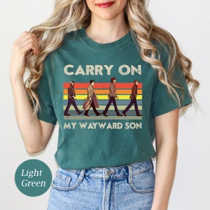 May include: A teal t-shirt with a retro design featuring four figures walking across a rainbow stripe with the text "Carry On My Wayward Son".