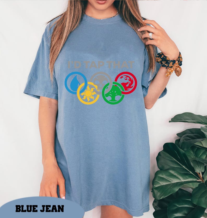 Pode incluir: Uma camiseta azul oversized com o texto "I'd Tap That" e um gr&aacute;fico de cinco s&iacute;mbolos m&aacute;gicos em um c&iacute;rculo.