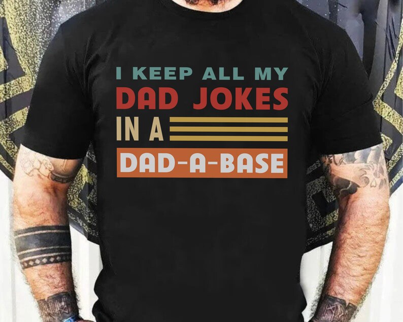 May include: Black t-shirt with a vintage-style graphic that reads "I keep all my dad jokes in a dad-a-base".