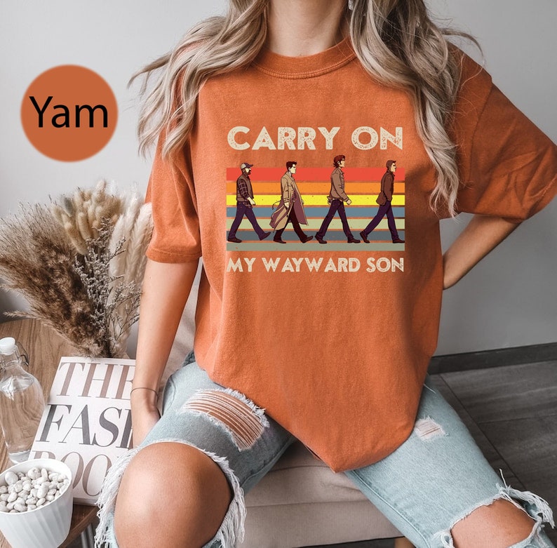 May include: Orange t-shirt with a retro graphic of four figures walking across a striped background. The text "Carry On My Wayward Son" is printed on the shirt.