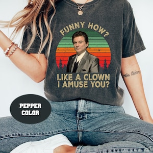 Puede incluir: Camiseta gris oscuro con el texto "FUNNY HOW? LIKE A CLOWN I AMUSE YOU?" sobre una imagen retro de un hombre con traje. La camiseta es de color pimienta.