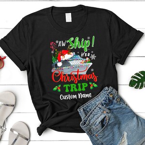 May include: Black t-shirt with a Christmas cruise ship design. The text reads "Aw Ship! It's a Christmas Trip" with a holly border and a space for a custom name.