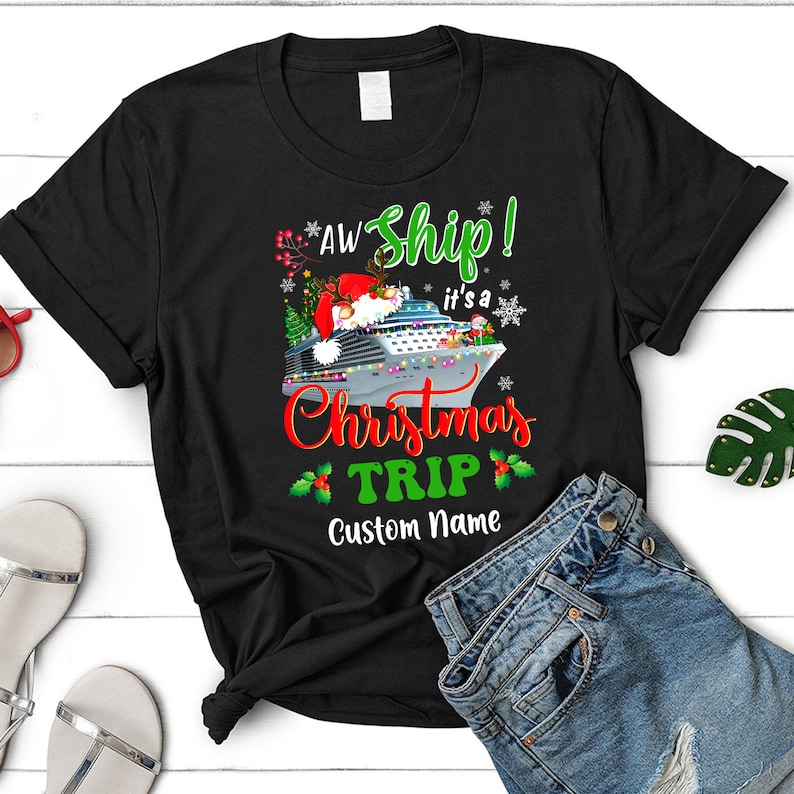 May include: Black t-shirt with a Christmas cruise ship design. The text reads "Aw Ship! It's a Christmas Trip" with a holly border and a space for a custom name.