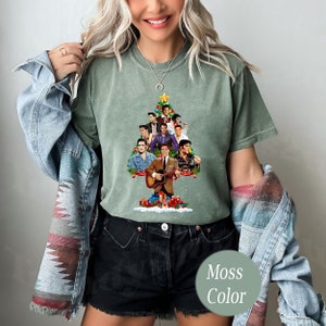 May include: A green t-shirt with a Christmas tree design featuring a collage of Elvis Presley images. The tree is decorated with red and white ornaments and a star on top. The text "Moss Color" is visible in the lower right corner of the image.