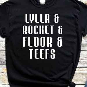 Peut inclure: T-shirt noir avec du texte blanc qui dit "LYLLA & ROCKET & FLOOR & TEEFS"