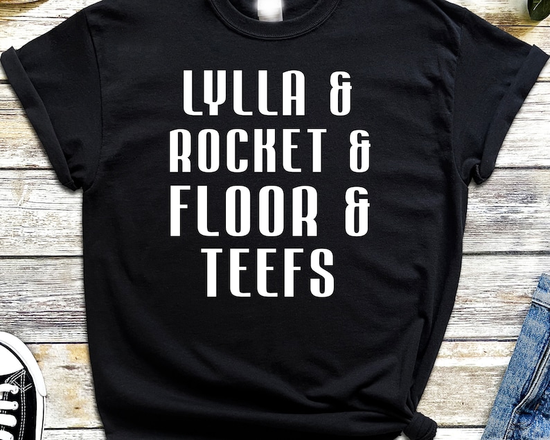 Peut inclure: T-shirt noir avec du texte blanc qui dit "LYLLA & ROCKET & FLOOR & TEEFS"