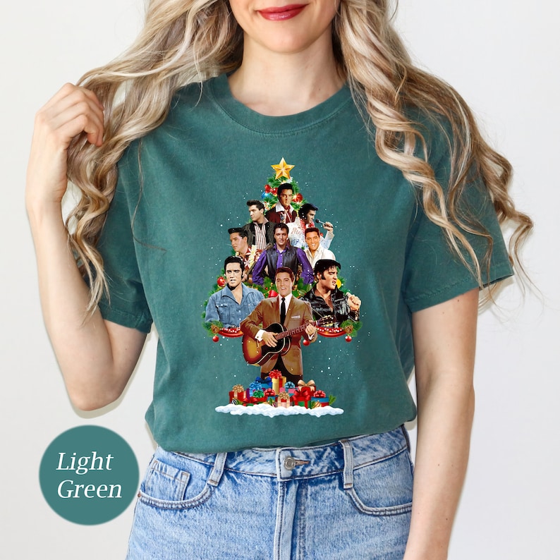 May include: A teal green t-shirt with a Christmas tree design featuring multiple images of Elvis Presley. The tree is decorated with red ornaments and a yellow star on top.