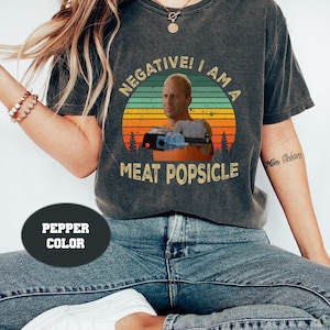 May include: A gray t-shirt with a vintage-style graphic of a man holding a gun. The graphic says "Negative! I am a Meat Popsicle".