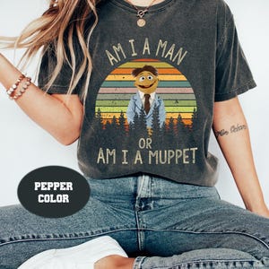 May include: A dark grey t-shirt with a vintage-style graphic of a character from the Muppets. The graphic features a sunset with the text "Am I a Man or Am I a Muppet".