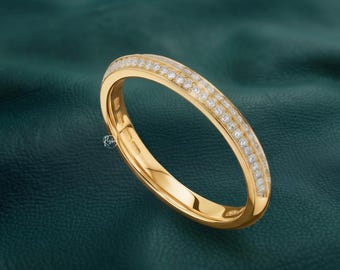 May include: A polished yellow gold band ring featuring a channel-set row of small, round, clear white diamonds along the outer surface. The interior of the band displays visible hallmarks and the small text Risha engraved on the metal.