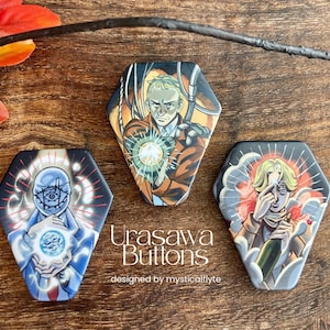 Puede incluir: Tres botones hexagonales Urasawa con ilustraciones de estilo anime. Los botones muestran personajes con orbes brillantes y diseños intrincados en tonos azules, naranjas y rojos. El texto "Urasawa Buttons" es visible.