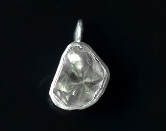 Puede incluir: Un colgante de plata con una piedra preciosa transparente y facetada de forma irregular.