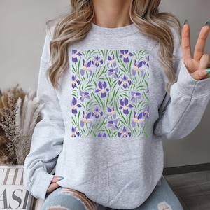 May include: A gray sweatshirt with a purple and green floral print. The print features a repeating pattern of stylized iris flowers.