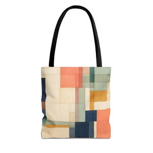 May include: A tote bag featuring a geometric pattern of intersecting lines and rectangular blocks in shades of coral, muted teal, mustard yellow, navy blue, and cream. The bag has two solid black fabric handles attached to the top edge.
