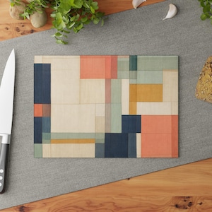 Puede incluir: Una tabla de cortar rectangular de cristal con un patrón de cuadrícula geométrica compuesto por bloques de varios tamaños en tonos azul marino, naranja apagado, amarillo suave, verde salvia y crema, con finas líneas negras.