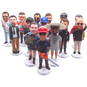 May include: A collection of bobblehead figurines of various people, each with unique outfits and accessories. The figurines stand on white circular bases with a logo. The bobbleheads are of different skin tones and hairstyles.