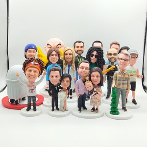 May include: A collection of custom bobblehead figurines, each depicting a person. The figurines vary in attire and accessories, including a wedding couple, a police officer, and a person in a sports jersey. The bobbleheads are on individual white bases.