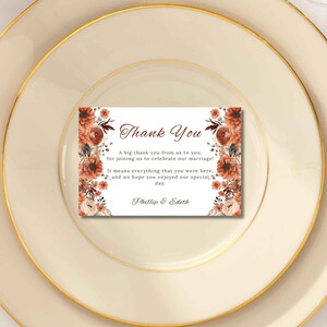 Könnte beinhalten: Eine rechteckige Dankeskarte mit floralen Akzenten, die die Worte "Thank You" in eleganter Schrift enthält. Die Karte enthält eine Dankesbotschaft und die Namen "Phillip & Edith". Die Karte liegt auf einem cremefarbenen Teller mit Goldrand.