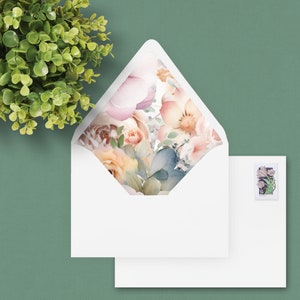 Könnte beinhalten: Ein weißer Umschlag mit einem Blumendesign auf der Klappe. Das Design zeigt rosa, pfirsichfarbene und blaue Aquarellblumen.