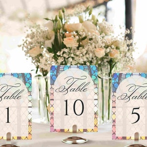 May include: Three table number cards with a stained glass design. The cards are white with black text that reads "Table 1", "Table 10", and "Table 5".
