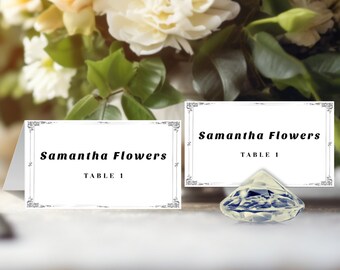 May include: Two white table cards with black text and a decorative border. The text reads "Samantha Flowers Table 1". A clear diamond-shaped table number holder sits on the table.