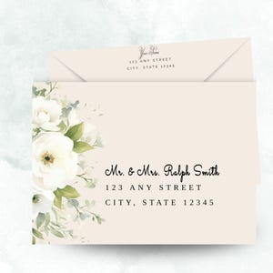 May include: Cream-colored stationery set featuring a floral design with white flowers and green leaves. The stationery includes an envelope and a card with the text "Mr. & Mrs. Ralph Smith" and address details.