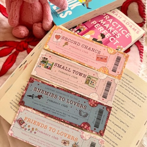 Puede incluir: Cuatro marcapáginas rosas y azules con un fondo brillante y letras doradas. Cada marcapáginas tiene un título diferente: "Second Chance", "Small Town", "Enemies to Lovers" y "Friends to Lovers". Cada título va seguido de las palabras "romance club".