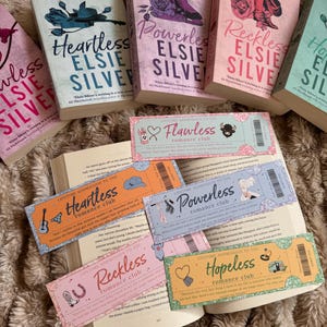 Peut inclure: Plusieurs romans d'amour d'Elsie Silver, tels que "Heartless" et "Powerless", sont présentés avec des couvertures colorées. Des billets décoratifs avec l'inscription "Romance Club" sont également visibles.