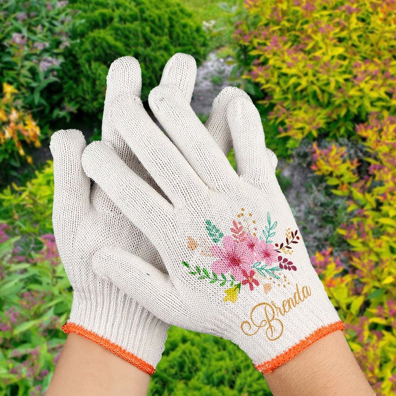 May include: White gardening gloves with an orange trim and a floral design. The gloves have the name "Brenda" written in gold script on the back.
