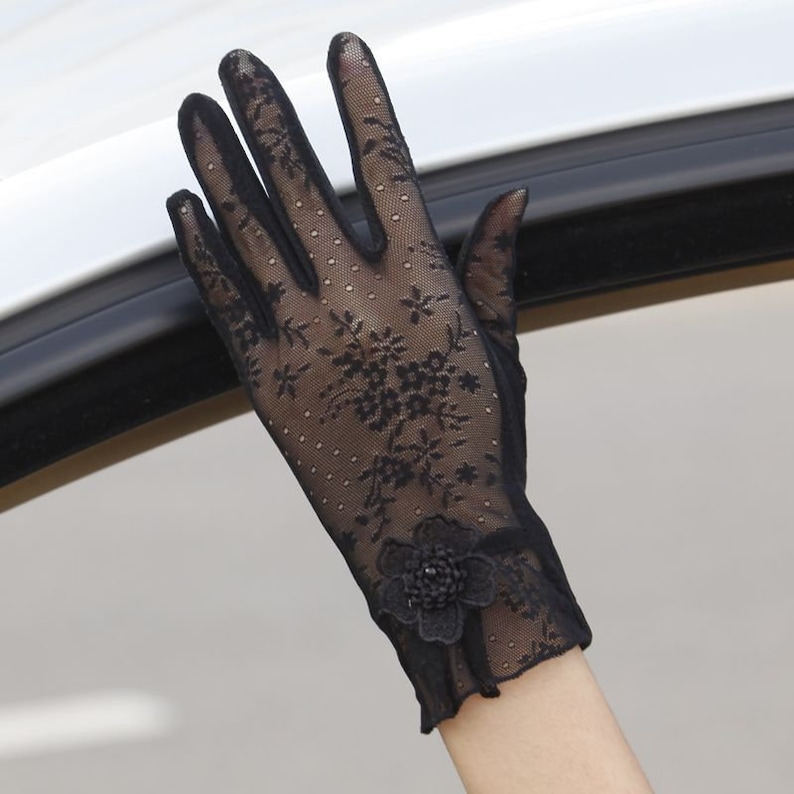 May include: Black lace gloves with a floral pattern and a black flower embellishment on the back of the hand.