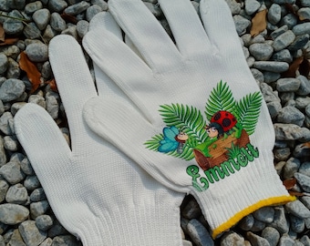 Op de afbeelding: Witte tuinhandschoenen met een kleurrijk insectenontwerp. Het ontwerp omvat een lieveheersbeestje, een vlinder en de naam "Emmett" in groen schrift. De manchetten hebben een gele rand.