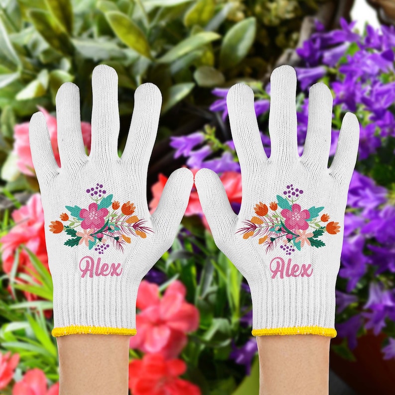 以下が含まれることがあります： 花柄のデザインと「Alex」という名前が刺繍された白いガーデニンググローブのペア